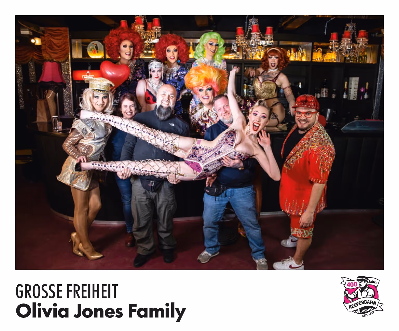 Gruppenfoto der Olivia Jones Family in einer Bar: Dragqueens und Gäste posieren gemeinsam, eine Person wird getragen.